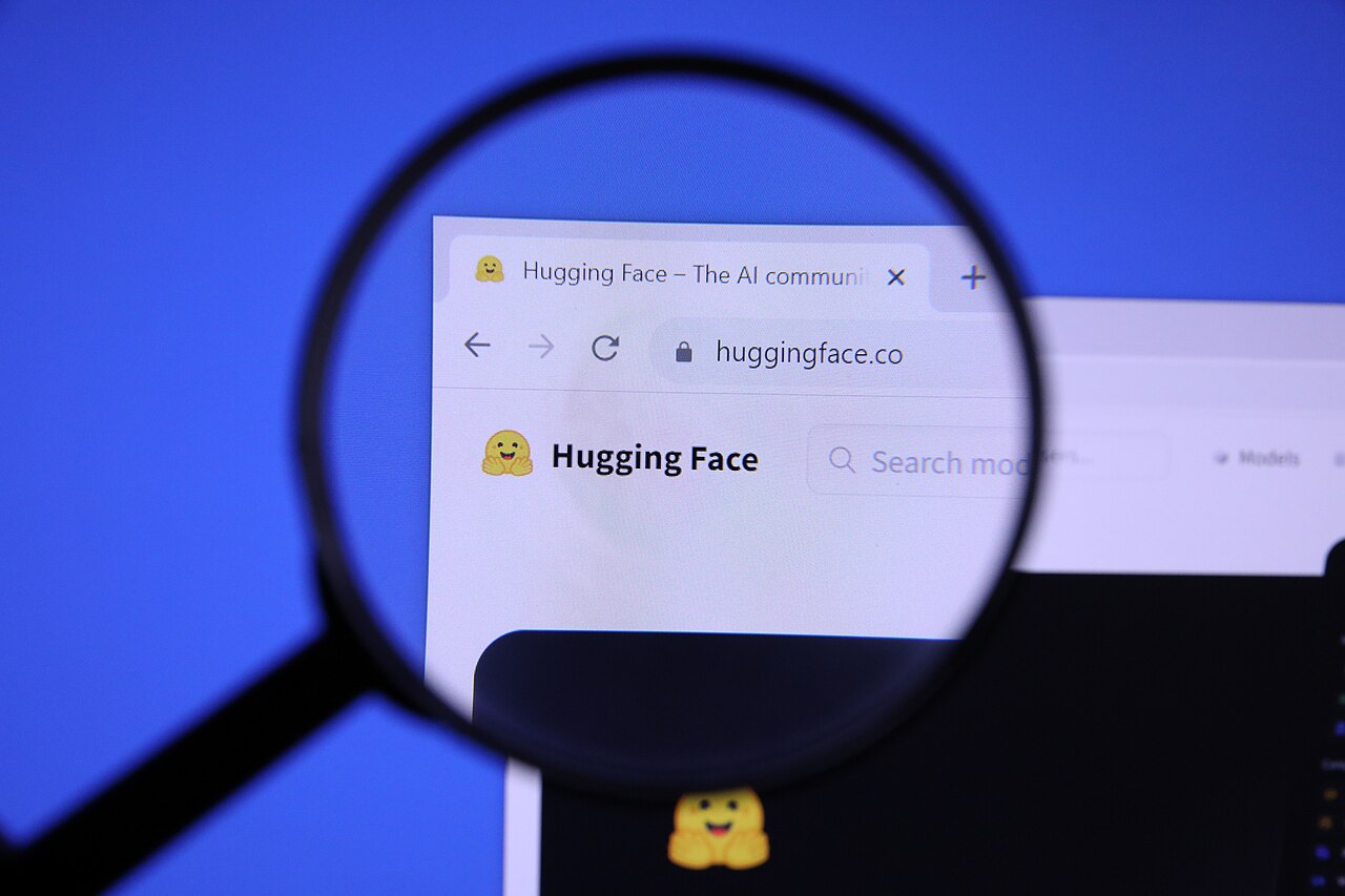 The Hugging Face website homepage viewed on a computer screen, magnified with a magnifying glass